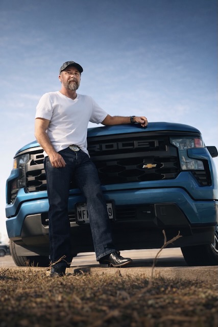 Michael Vowell standing beside a blue Chevrolet truck under an open sky